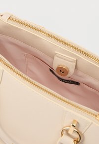 Μπεζ τσάντα χειρός με υφή στην εξωτερική επιφάνεια, χρυσό φερμουάρ και ροζ υφασμάτινη επένδυση. Διαθέτει κλείσιμο με κουμπί και εσωτερική τσέπη.