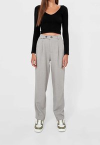 Pantalons gris taille haute avec plis, en tissu léger. Associés à un haut noir à manches longues et des baskets avec des accents verts.