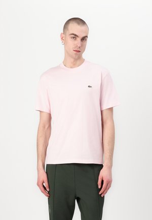 Pink cotton t-shirt with crew neck and short sleeves, featuring a small green logo on the left chest. Minimalist design, smooth texture.