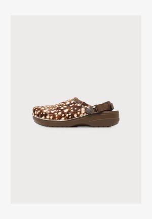 Brun- og hvidplettet slip-on-træsko med justerbar bagrem og tekstureret sål for greb, vist fra siden på en hvid baggrund.