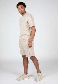 Beige bavlněná trička a šortky se malým vyšitým vzorem na šortkách. Kombinujte s světlými šedými sportovními botami. Jednoduchý, neformální styl.