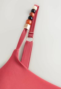 Sangle en tissu rouge avec des perles décoratives en crème, noir, marron, et un détail anneau doré sur un fond clair.