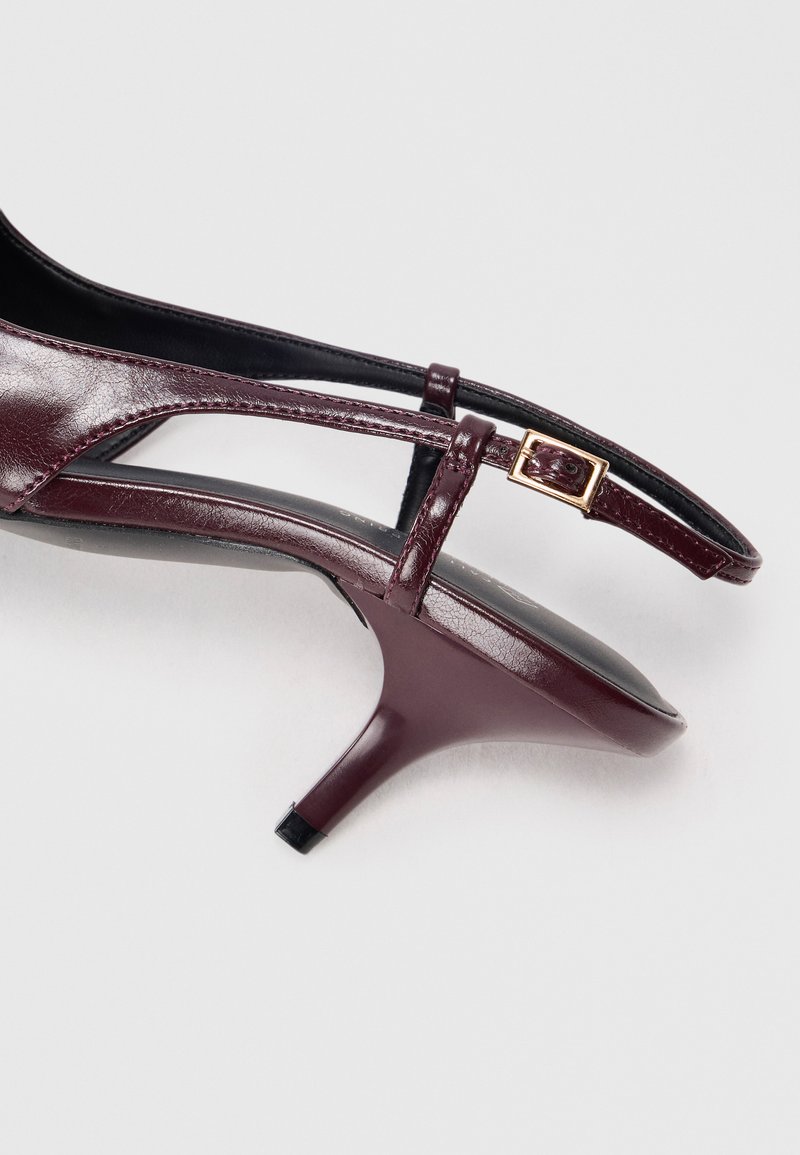 Chaussure slingback en cuir violet foncé avec un petit talon kitten et une petite boucle dorée sur la sangle, sur fond blanc.