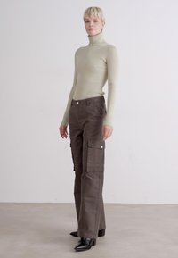 Béžový žebrovaný rolák, slim fit. Hnědé cargo kalhoty s několika kapsami a stříbrnými knoflíkovými detaily. Černé boty na jehlovém podpatku.