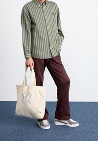 Grön- och vitrandig skjorta med knappar, vinröda byxor och en beige tygkasse med marinblå NY-logotyp, kombinerat med grå sneakers.