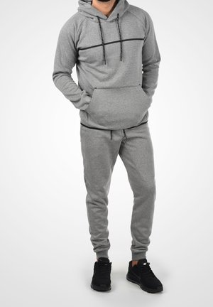 Graues Kapuzenpullover- und Jogginghosen-Set mit Kordelzugkapuze, Fronttasche und schwarzen Akzentlinien; weicher Stoff, schmal zulaufende Passform, kombiniert mit schwarzen Turnschuhen.