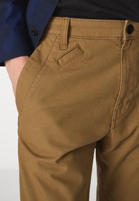 Bruna bomullbyxor med en slät textur. Funktioner inkluderar en sidoficka och hållbar sömnad. Kombineras med en skjorta i marinblått rutmönster.