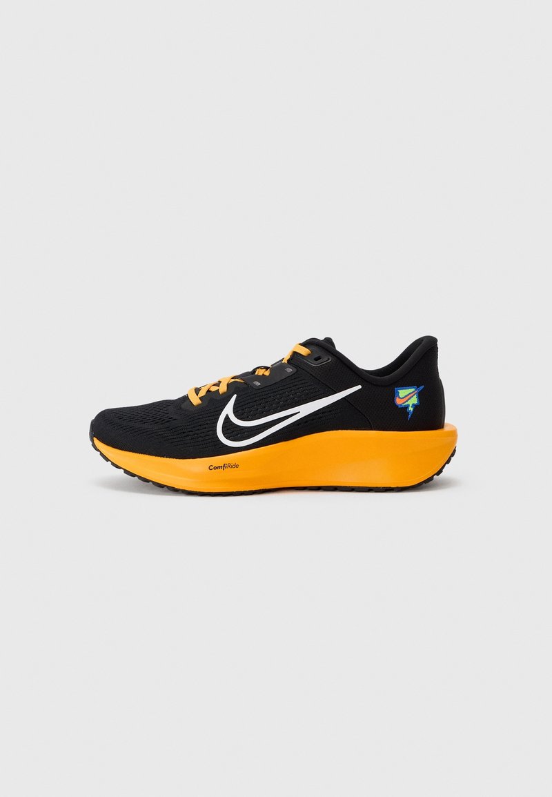 Chaussure de sport noire avec un dessus texturé, semelle orange et lacets noirs. Logo blanc notable et accent coloré à l'arrière.