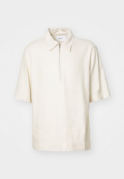 Chemise crème à manches courtes avec fermeture éclair et col classique, confectionnée dans un tissu doux, présentant une coupe décontractée et un design minimaliste.