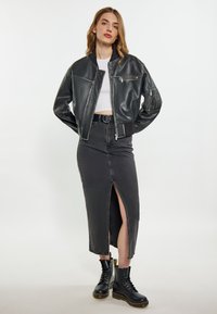 Giacca bomber nera in pelle con tasche con zip, abbinata a una gonna in denim nera con spacco alto e stivali neri con lacci, che mostra un design minimalista.