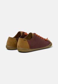 Sneaker in pelle marrone e bordeaux con lacci arancioni, punta tondeggiante, texture morbida e suola flessibile. Il logo è visibile sul tallone.