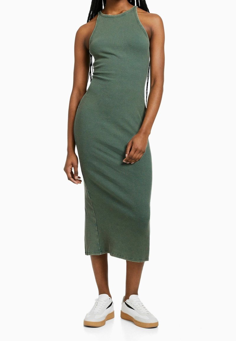 Abito midi verde a coste con collo alto e spacchi laterali, abbinato a sneakers bianche con dettaglio nero e suola in gomma.