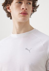 Valge puuvillane T-särk, millel on rindkeres peen hall Puma logo, klassikalise ümara kaeluse ja raglanvarrukatega.