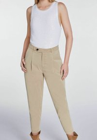 Haut sans manches blanc avec une finition texturée en sequins, associé à un pantalon taille haute beige clair avec des plis avant et une fermeture à bouton.