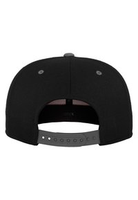 Fekete snapback sapka, egyenes dizájnnal, sima textúrával és a hátulján állítható műanyag pánttal. Finom varrási részletek találhatóak rajta.