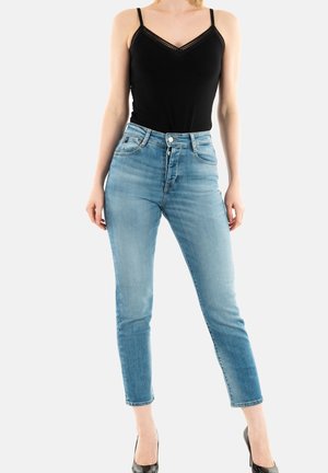 Jeans azules de cintura alta con un ajuste slim, diseño de cinco bolsillos y un ligero desgastado. Combinados con una camiseta sin mangas negra con detalles de encaje.