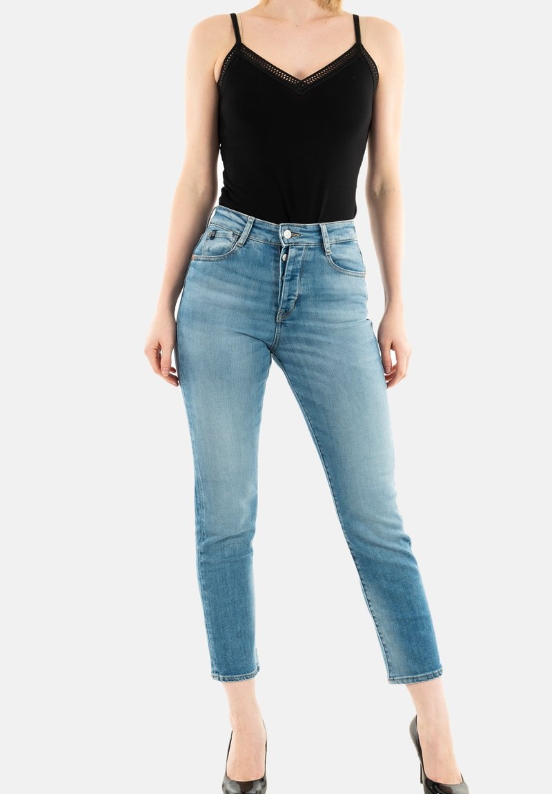Jeans azules de cintura alta con un ajuste slim, diseño de cinco bolsillos y un ligero desgastado. Combinados con una camiseta sin mangas negra con detalles de encaje.