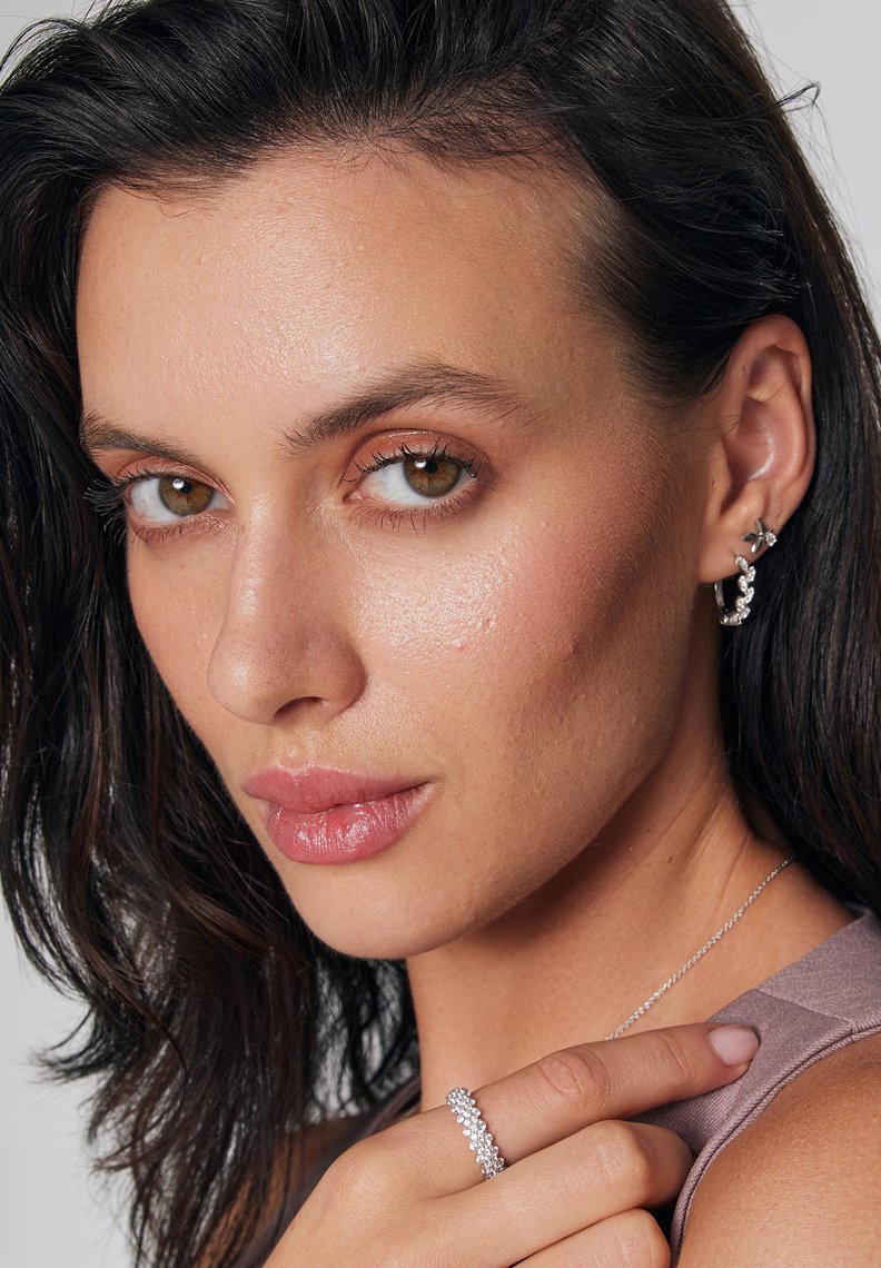 Srebrne kolczyki w kształcie kół oraz błyszczący pierścionek z kwiatowym wzorem, noszone przez osobę z długimi, ciemnymi włosami i jasną skórą.