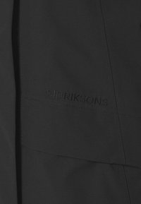 Tessuto nero con cuciture sottili impunturate e logo in rilievo "DIDRIKSONS" ricamato con filo nero coordinato.