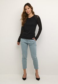 Černý top s dlouhým rukávem a krajkovými detaily na rukávech, spárovaný se světle modrými slim-fit kalhotami a černými vysokými podpatky. Jednoduchý, přiléhavý design.