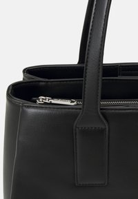 Czarna skórzana torba o gładkiej fakturze, z dwoma uchwytami i zamykaną na zamek kieszenią z detalami w kolorze srebrnym.