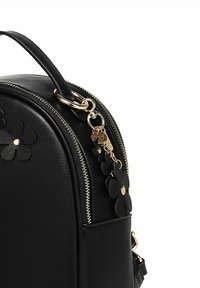 Černý kožený batoh se zlatým zipem a černými květinovými přívěsky připevněnými k hornímu uchu.