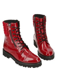 Paire de bottes rouges brillantes à lacets, avec semelles noires et fermetures éclair latérales, équipées de cols rembourrés autour de la cheville et de semelles robustes.