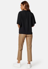 Top corto nero con dettagli plissettati sul retro, abbinato a pantaloni skinny in ecopelle color cammello e sneaker bianche.