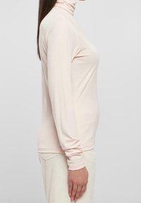 Helles rosa Langarm-Turtleneck-Oberteil aus weichem, dehnbarem Stoff. Verfügt über eine schmale Passform und eng anliegende Ärmel, mit einem schlichten, glatten Design.