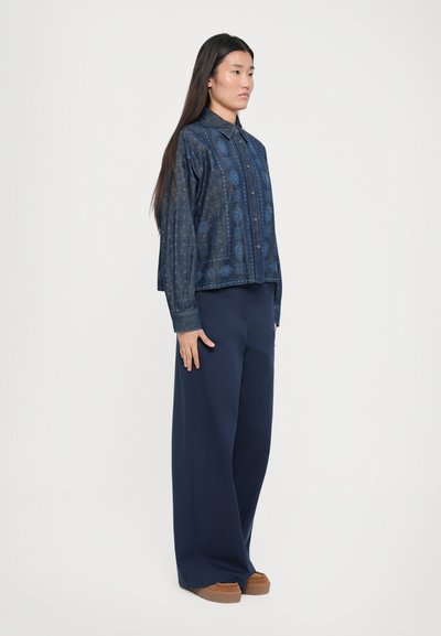 Denim shirt with blue patterned design, collared neck, front buttons, paired with navy wide-leg trousers and brown platform shoes.
