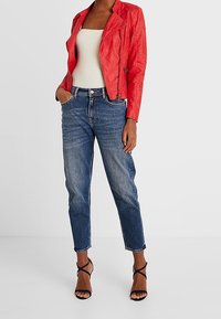 Giacca da moto rossa in pelle con un design aderente, canotta bianca, jeans in denim e tacchi neri con cinghie. Outfit urbano casual.