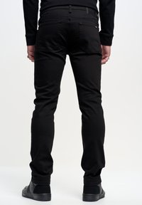 Jeans in denim nero con vestibilità slim, dotati di tasche posteriori e una vita testurizzata, abbinati a scarpe slip-on nere.