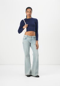 Navy long-sleeve crop top, light blue flared jeans, and a small pink handbag. The jeans feature a classic five-pocket design.