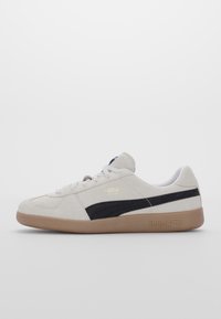 Sneakers in suede grigio con una striscia in suede nero, lacci bianchi e suola in gomma color beige. Presentano un logo dorato sul lato e dettagli testurizzati.