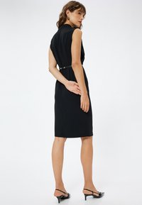 Schwarzes ärmelloses Kleid mit einer taillierten Silhouette, mit einem Gürtel in der Taille, glatter Textur, knielangem Saum und minimalistischen Designelementen.