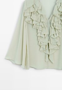 Jasnozielona bluzka z warstwowymi falbanami przy dekolcie i zapięciu. Miękka, swobodna tkanina z otwarciem w kształcie litery V. Elegancki design.