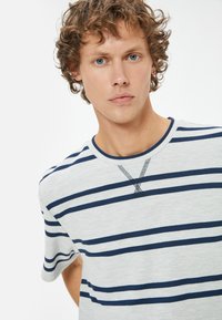 Randig kortärmad skjorta i ljusgrått med marinblå horisontella ränder, rund halsringning med en strukturerad detalj vid kragen.