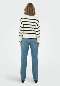 Svītraina džemperis krēmkrāsā un melnā krāsā ar ribotu tekstūru, kombinēts ar augsta vidukļa ziliem džinsiem. Raksturots ar brīvu piegriezumu un apaļu kakla izgriezumu.