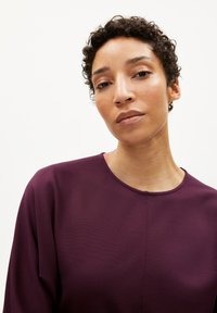 Lila Oberteil mit runder Ausschnitt, aus einem strukturierten Stoff gefertigt. Besitzt subtile Nähte und einen lässigen Schnitt. Nahaufnahme des Oberkörpers.