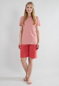 T-shirt à rayures rouges et blanches avec des manches courtes, associé à un short rouge uni arrivant au genou. Fabriqué en coton doux et léger.