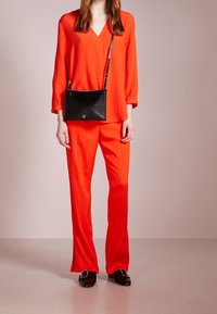 Czerwona bluzka z dekoltem w serek i długimi rękawami, zestawiona z pasującymi czerwonymi spodniami o szerokich nogawkach. Czarna torebka na ramię i błyszczące czarne buty dopełniają stylizację.