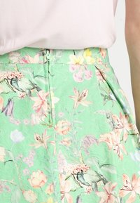 Jupe florale verte avec un motif texturé de fleurs roses, jaunes et blanches ; fermeture éclair au dos ; coupe ajustée avec plis.