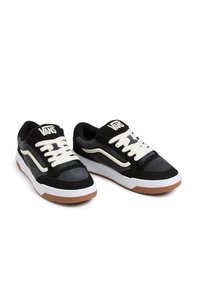 Sapatilhas de camurça e couro pretas com atacadores brancos, sola de borracha castanha e logotipo da Vans na língua e na lateral. Apresenta um colarinho acolchoado.