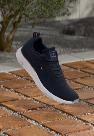 Navy blue athletic shoe with textured upper, white sole, and red/white/blue logo accents on the tongue and heel. Lightweight and flexible design.