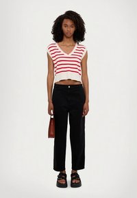 Bijeli kratki top s crvenim vodoravnim prugama, V-izrez, u kombinaciji s crnim širokim hlačama. Uključena smeđa torba i crne sandale na platformu.