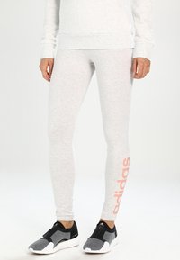 Jasnoszare legginsy z elastycznego materiału, o dopasowanym kroju, z wyraźnym różowym logo "adidas" na lewej nodze.