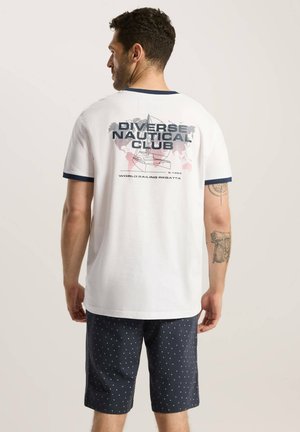 Biała koszulka z krótkim rękawem z granatowymi akcentami i graficznym nadrukiem z napisem "Diverse Nautical Club". Noszona z granatowymi szortami w małe białe kropki.