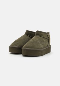 Olijfgroene suède enkelboots met een chunky platformzool, ronde neus en subtiele stiksels langs de bovenkant en zijkanten.