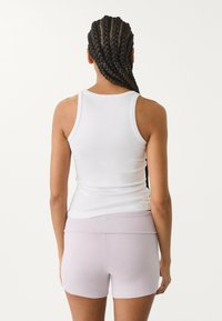 Weißes, tailliertes Top mit dünnen Trägern, kombiniert mit hellen lavendelfarbenen, hochgeschnittenen Shorts aus weichem Stretchstoff.