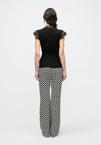 Czarna bluzka z koronkowym wykończeniem i krótkimi, falbaniastymi rękawkami, zestawiona ze spodniami z wysokim stanem i szerokimi nogawkami w wyrazisty czarno-biały geometryczny wzór.